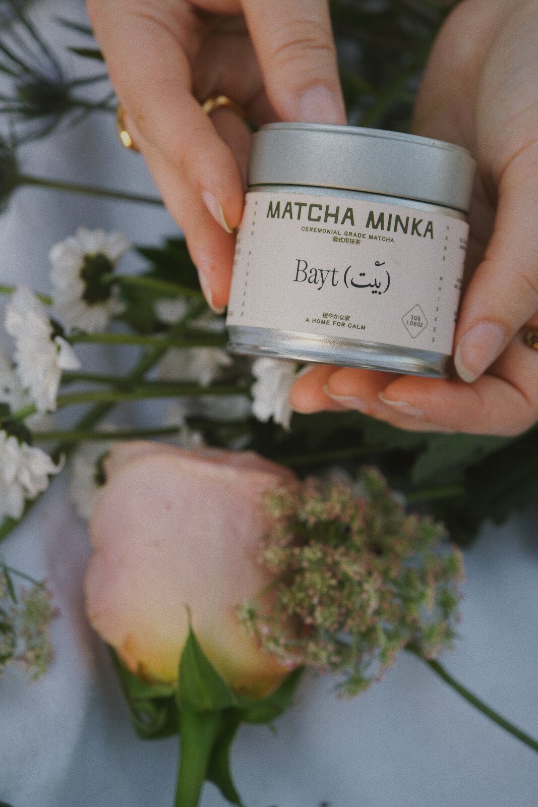 Hands holding the Matcha Minka ceremonial matcha tin with white flowers
