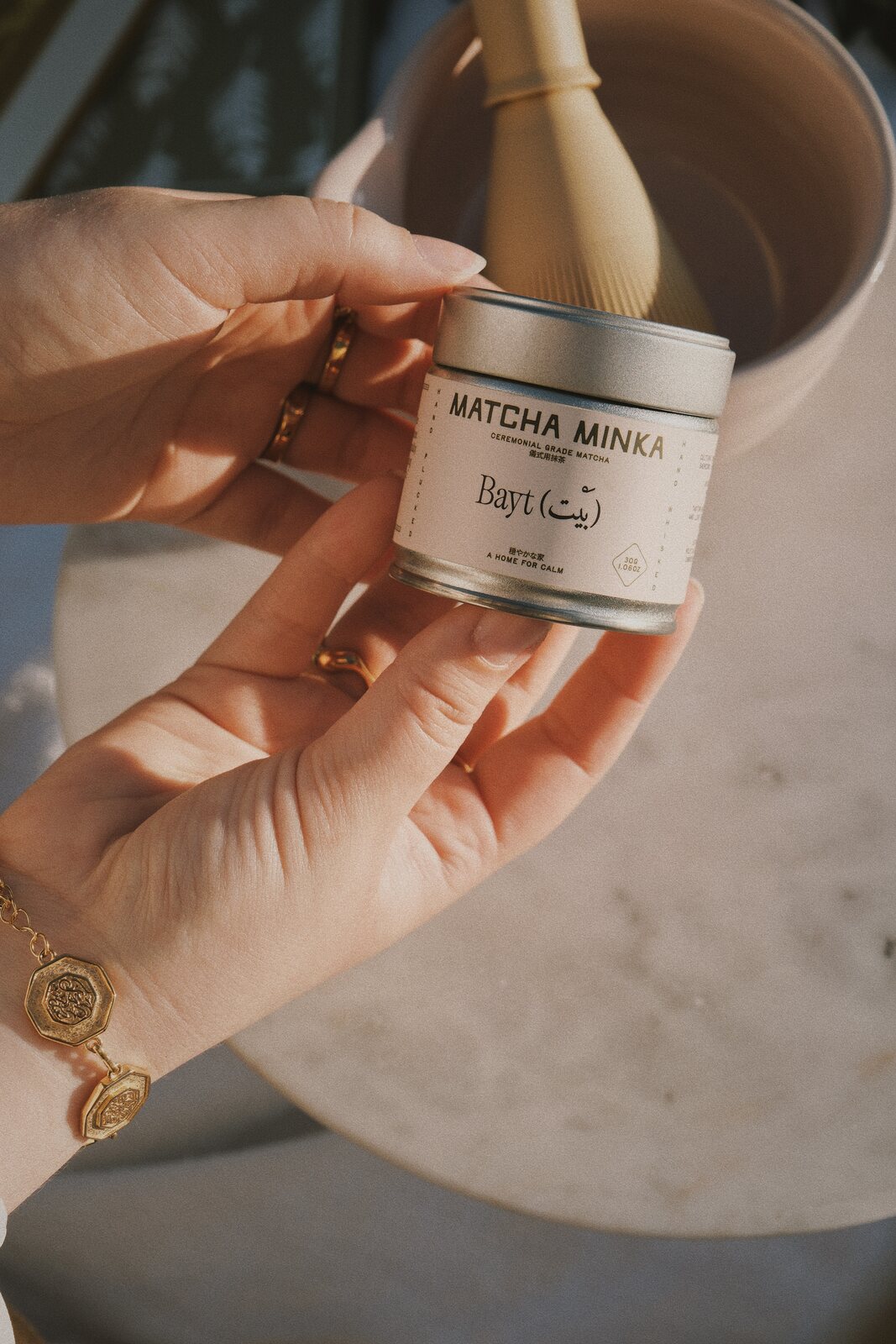 Hands holding the Matcha Minka tin with a chasen whisk