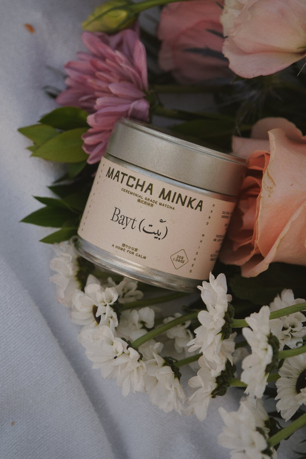 Matcha Minka tin among pink and white flowers